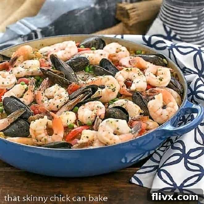 Julia Child's Paella a l'Americaine in a beautiful blue paella dish, garnished with fresh parsley and lemon wedges.