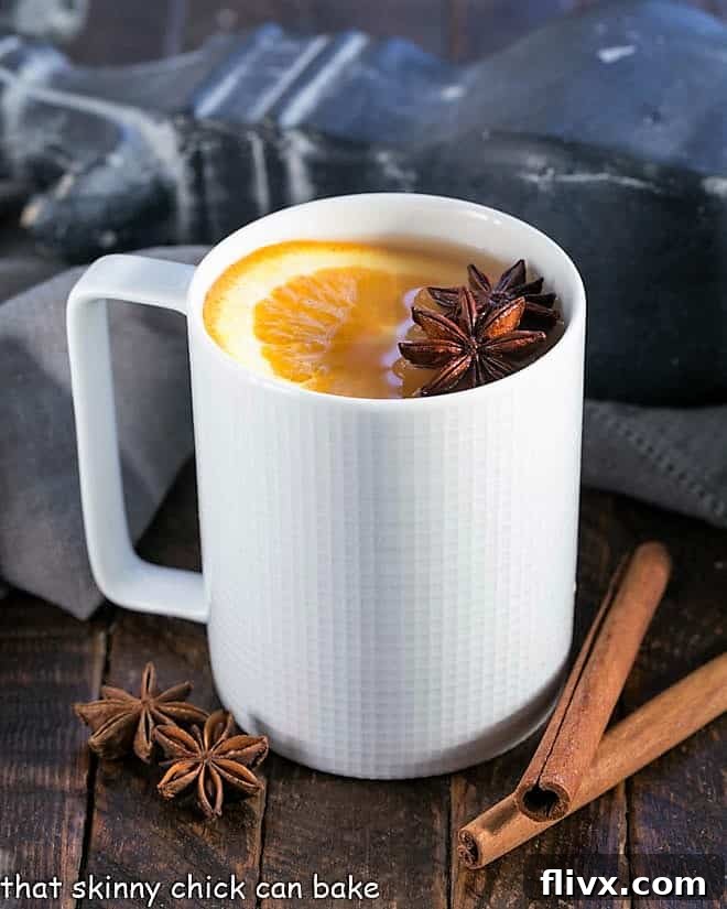 A cozy white mug filled with hot mulled apple cider, garnished with a vibrant orange slice and a cinnamon stick, ready to be enjoyed in autumn or winter.