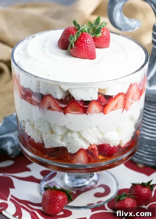 A close-up shot of the Strawberry Cheesecake Trifle showcasing its beautiful layers, topped with three vibrant strawberries for garnish.