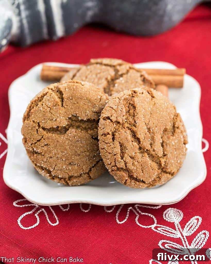 Three perfectly crinkled, chewy gingersnaps artfully arranged on a square white plate, hinting at their soft texture and rich spice.