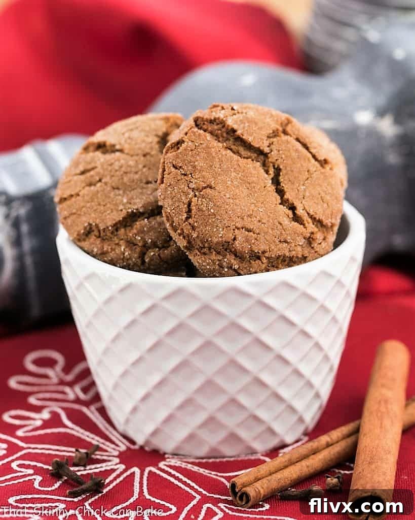 A bowl of freshly baked chewy gingersnaps, garnished with cinnamon sticks and whole cloves, highlighting the festive spices.