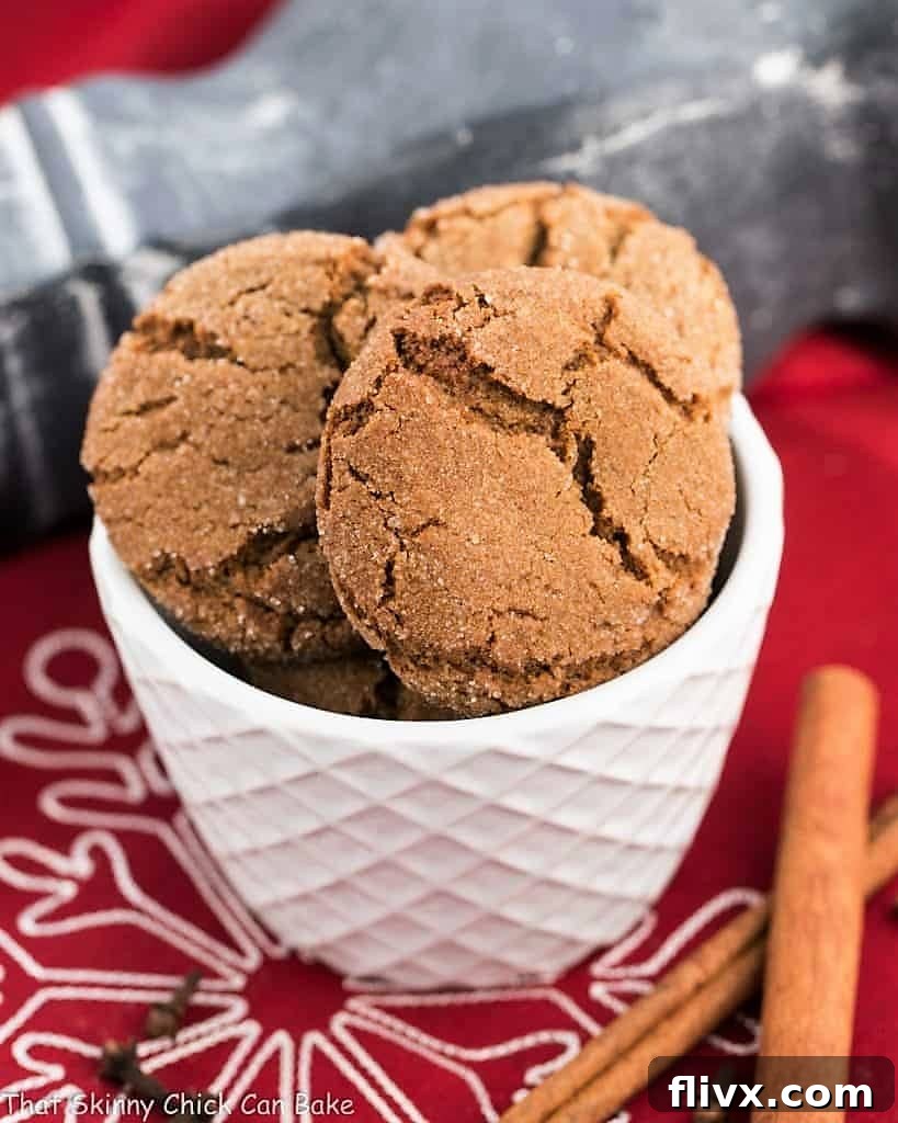 A cluster of chewy gingersnaps nestled in a white ceramic bowl, showcasing their beautiful crinkled texture and inviting warmth.