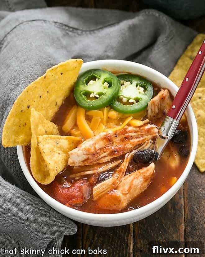 Slow Cooker Chicken Enchilada Soup in a white ceramic bowl garnished with chips and cheese.