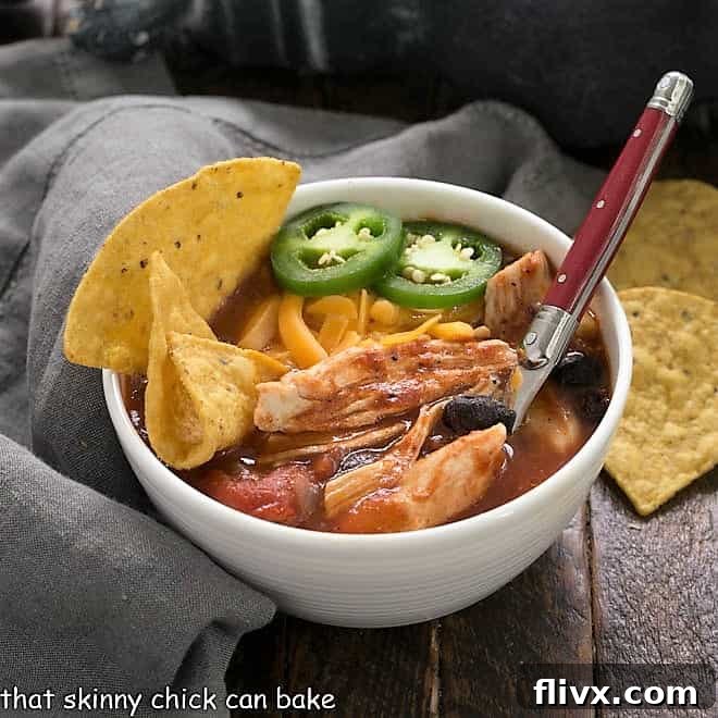 Enchilada soup in a white bowl with tortilla chips to garnish and a red handle spoon