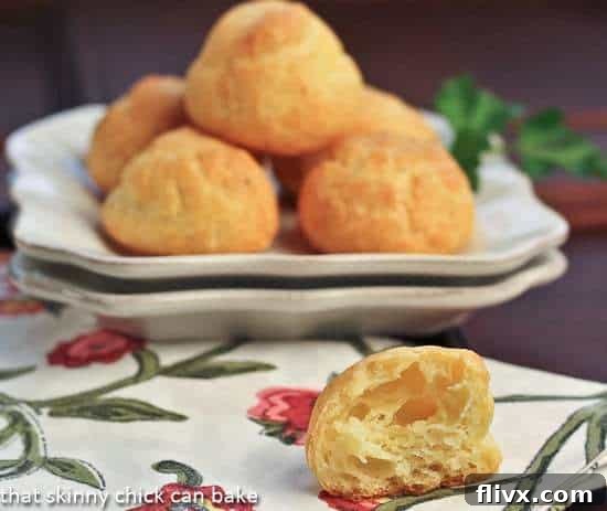 Golden Parisian Cheese Puffs artfully arranged on a white plate, with one puff broken open to reveal its airy interior, set against a blurred background