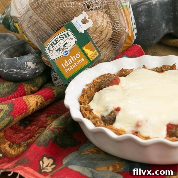 A close-up of a slice of Italian Poutine Pie, showcasing the hash brown crust, meatballs, marinara, and melted mozzarella.
