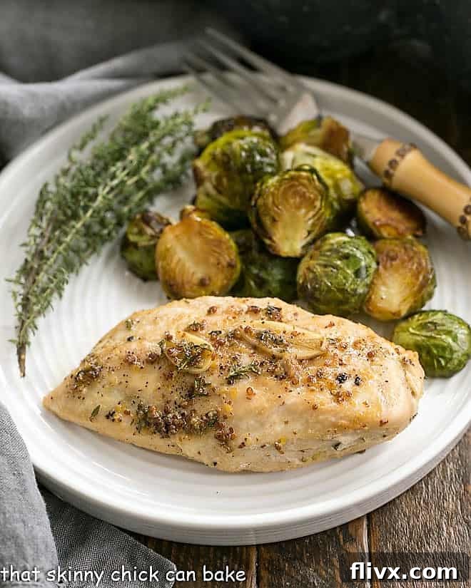 Maple-Glazed Chicken served on a white dinner plate with roasted Brussels sprouts and a sprig of thyme