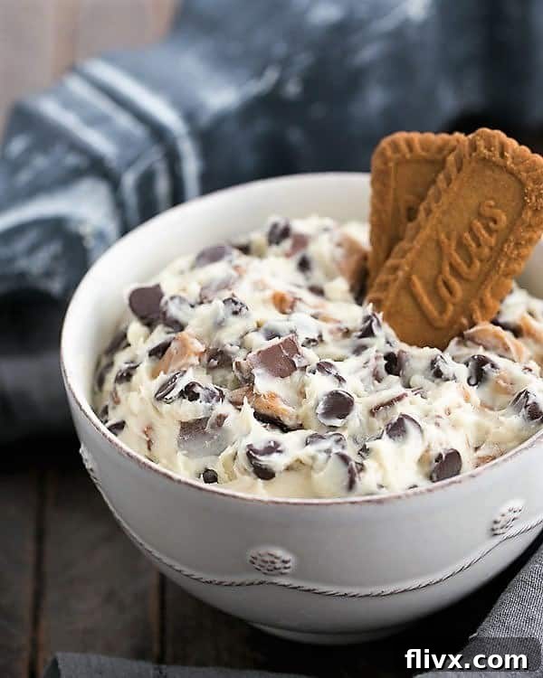 A simple white ceramic bowl brimming with a generous serving of Chocolate Chip Cookie Dough Dip, showcasing its creamy texture and visible chocolate and toffee pieces.