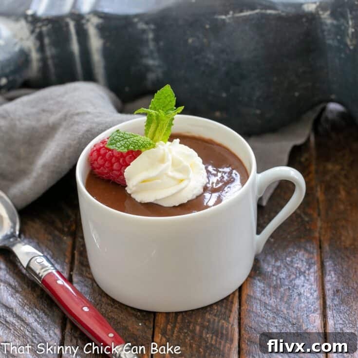 A charming teacup filled with luscious chocolate pots de creme, elegantly topped with a fresh raspberry and a swirl of light whipped cream, ready to be savored.