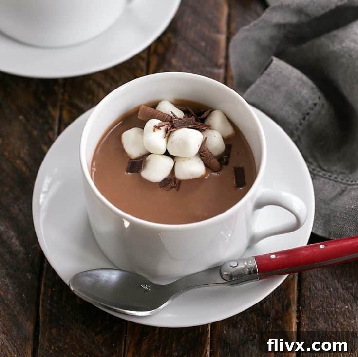 Cioccolata Calda in a white ceramic cup on a saucer with a red handled spoon and marshmallow garnish