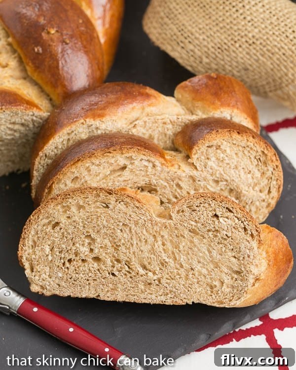 Three slices of Whole Wheat Challah on a slate tray with a red-handled butter knife, ready to be served.
