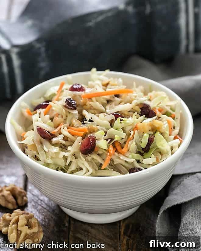 Easy coleslaw recipe in a small white ceramic bowl with a gray napkin and walnut halves, emphasizing its deliciousness and simple elegance.