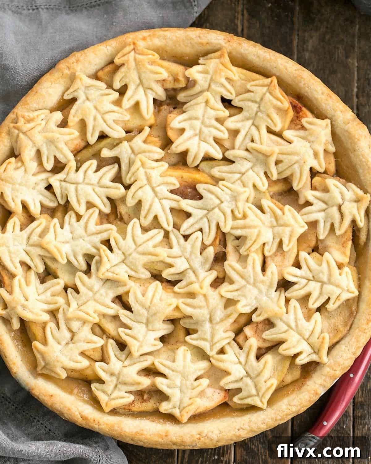 Overhead view of apple pie with a leaf topping and a red handle knife, ready to be sliced.