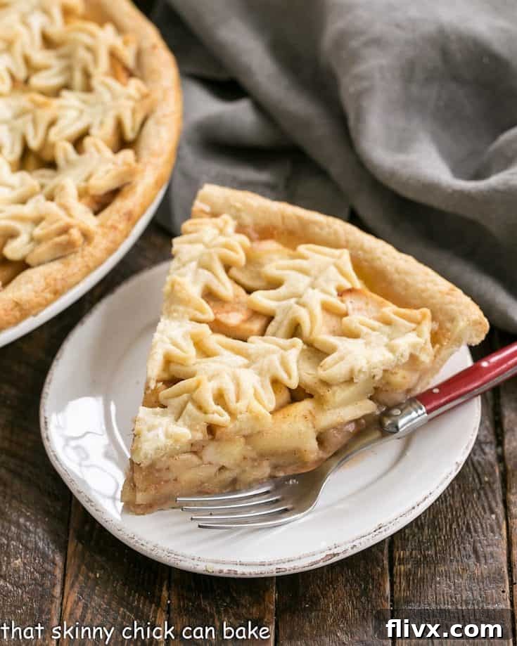 Slice of apple pie on a round white plate with a red handled fork