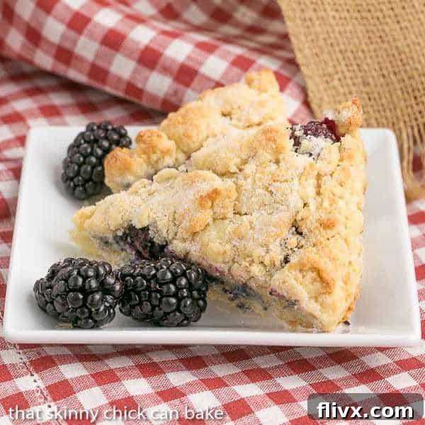 Freshly baked Blackberry Scones, golden brown and glistening with a hint of cream, arranged beautifully on a white square plate, ready to be served for a delightful breakfast or brunch. Each scone is visibly packed with juicy blackberries.