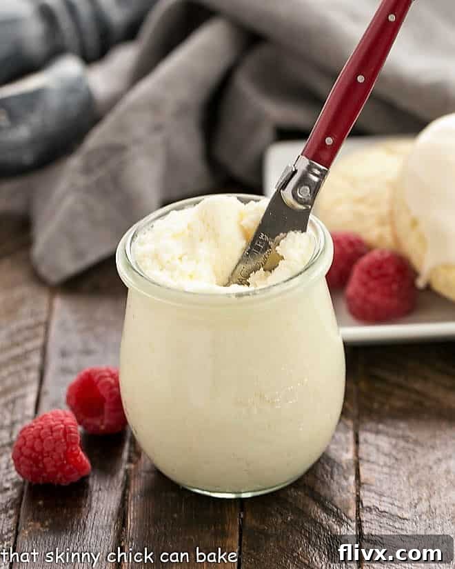 A beautiful jar of Instant Pot Clotted Cream, rich and creamy, with a red-handled knife resting nearby. Ready to be spread on warm scones for a delightful British tea experience.