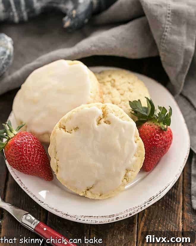Three perfectly baked vanilla bean scones arranged on a pristine white plate, accompanied by vibrant fresh strawberries. A classic pairing for a delicious cream tea.