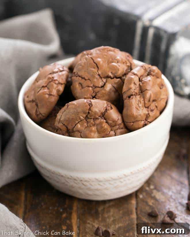 A white serving bowl overflowing with perfectly baked Chocolate Brownie Cookies, each one glistening with mini chocolate chips, promising a rich, fudgy texture.
