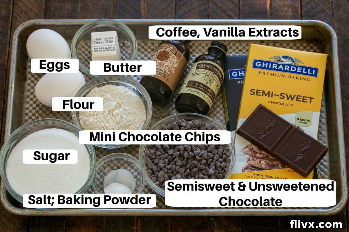 A neatly organized collection of ingredients for Chocolate Brownie Cookies, including chocolate bars, butter, eggs, sugar, and flour, laid out on a metal sheet pan with small labels.