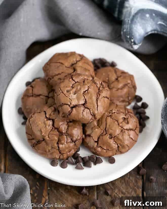 A stack of warm, glistening Chocolate Brownie Cookies, generously adorned with mini chocolate chips, resting on a white plate and ready to be enjoyed.