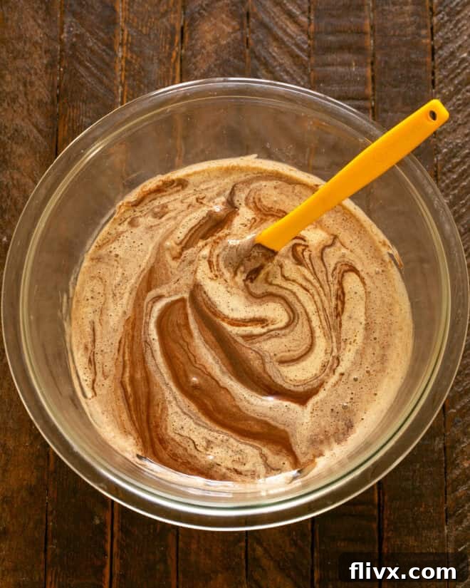 The rich, melted chocolate mixture being carefully folded into the light, airy egg mixture.