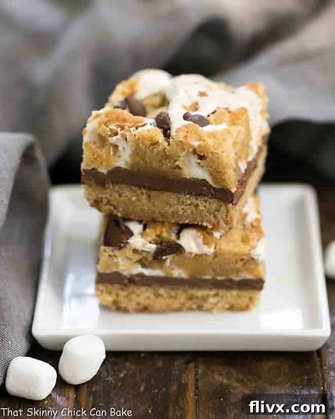 S'mores Cookie Bars stacked on a white plate, showcasing layers of graham cracker, chocolate, and marshmallow.