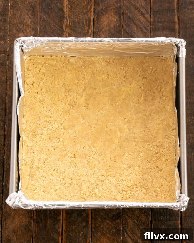 Pressing half of the cookie dough into the bottom of a prepared baking pan.