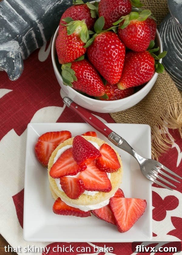 Overhead view of perfectly portioned olive oil cake rounds, each crowned with a generous swirl of sweetened whipped cream and adorned with glistening, ripe strawberry slices, showcasing an inviting dessert.