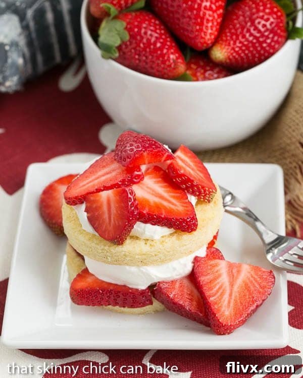 A close-up shot of a plate featuring several perfectly formed fresh Strawberry Shortcakes, each made with golden-hued Olive Oil Cake rounds, generously adorned with vibrant red strawberries and white whipped cream.