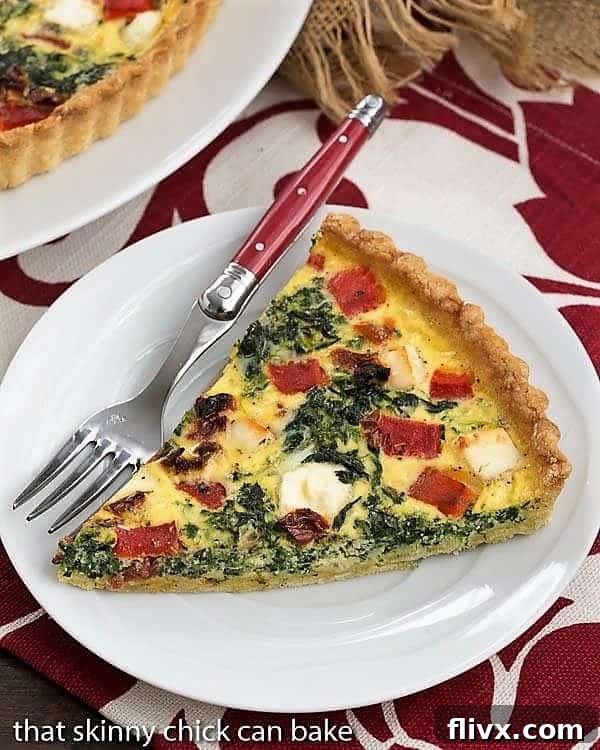 A delicious slice of Sun-dried Tomato and Spinach Quiche on a white plate, resting on a red and white checkered napkin, highlighting its rustic charm.