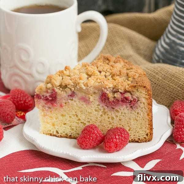 A slice of raspberry coffee cake on a white plate with two fresh raspberries garnish