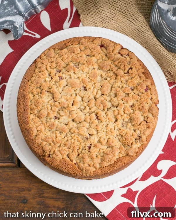 Overhead view of raspberry coffee cake on a white serving plate, showing berries and streusel