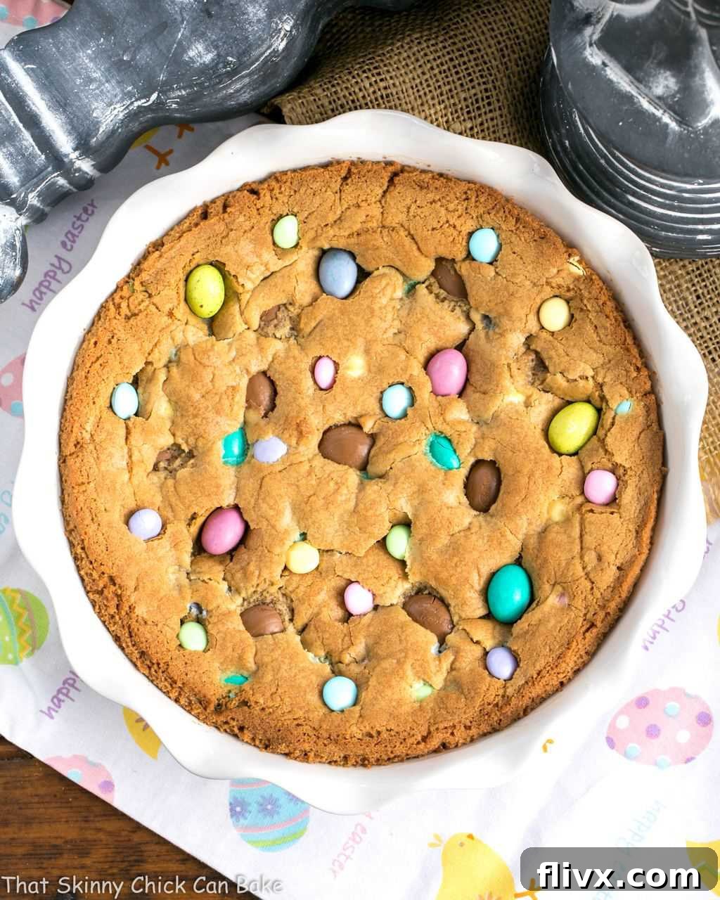 An overhead image showcasing a large, round Easter cookie cake beautifully studded with various types of vibrant Easter candy and chocolate chips.