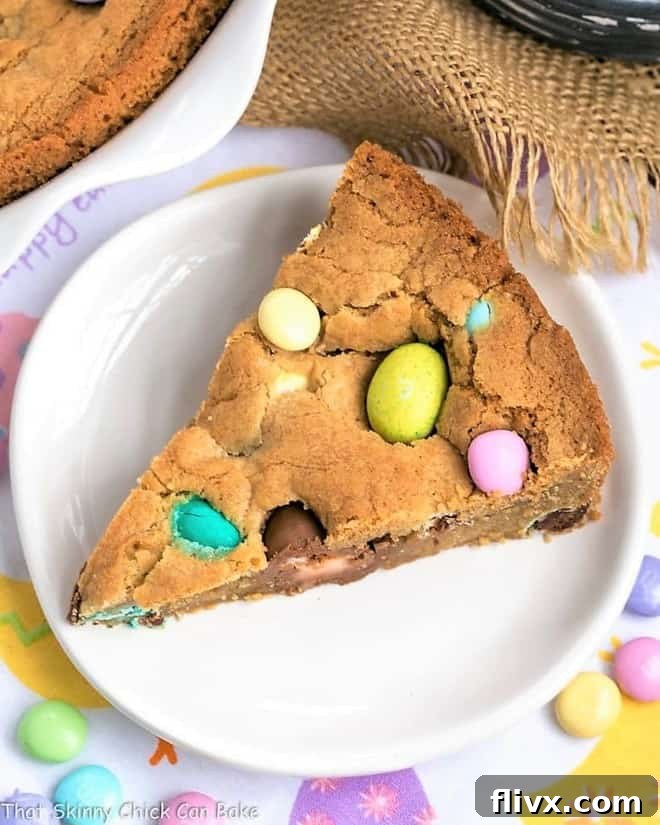 A single, perfectly cut slice of homemade Easter cookie cake resting on a pristine white dessert plate, highlighting its chewy texture and colorful candy inclusions.