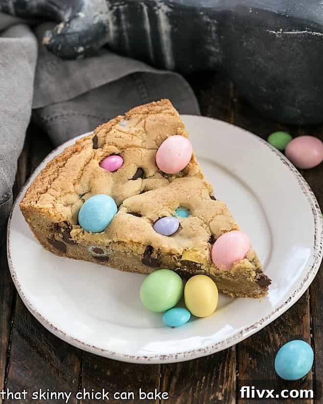 A beautifully presented slice of Easter cookie cake, adorned with colorful candies, on a white dessert plate