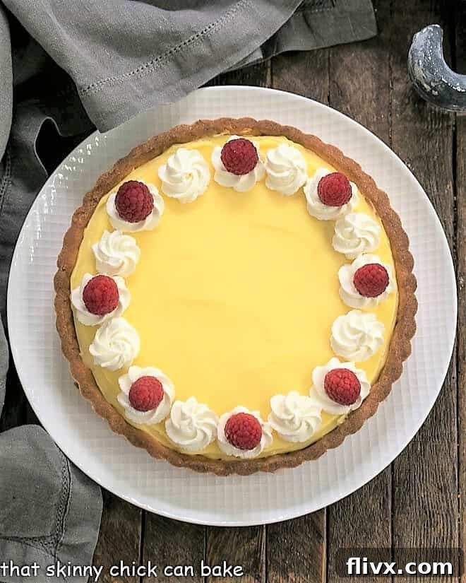 Overhead view of Creamy Lemon Tart on a white plate, garnished with fresh lemon slices and mint leaves, highlighting its smooth, glossy surface and golden crust.