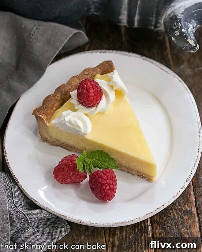 A perfectly sliced piece of Creamy Lemon Tart on a white dessert plate, showing the smooth filling and flaky crust.