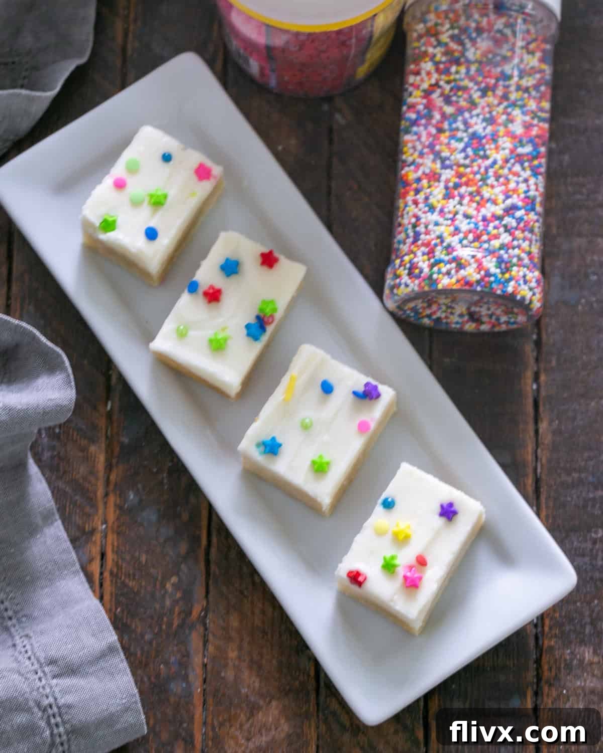 A large batch of freshly baked Frosted Sugar Cookie Bars, with a thick layer of frosting and colorful sprinkles, arranged beautifully on a white ceramic tray.