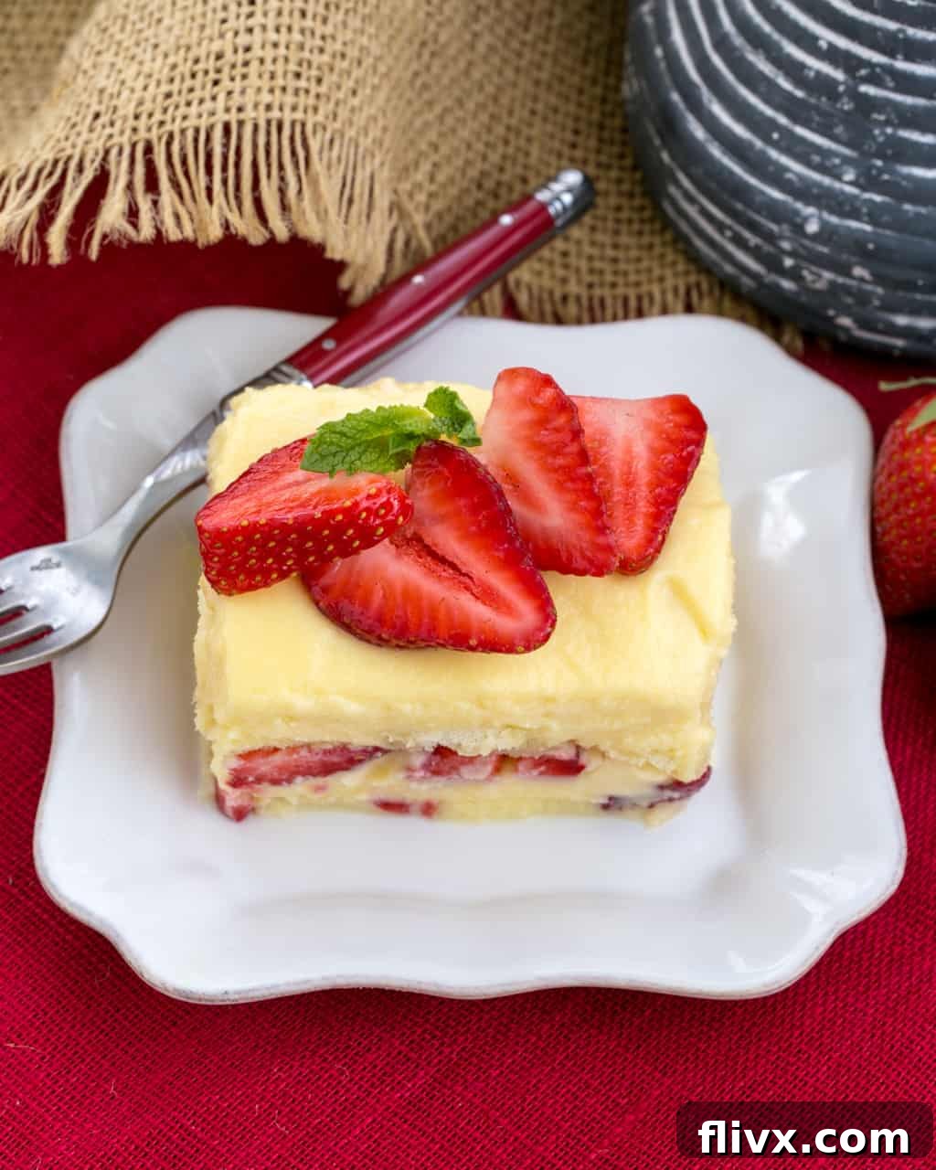 Berry Tiramisu with Grand Marnier - A strawberry twist on the Italian classic with mascarpone and Grand Marnier soaked ladyfingers! A perfectly sliced piece of Berry Tiramisu with Grand Marnier on a square white plate, accompanied by a red-handled fork. Fresh strawberries adorn the top.