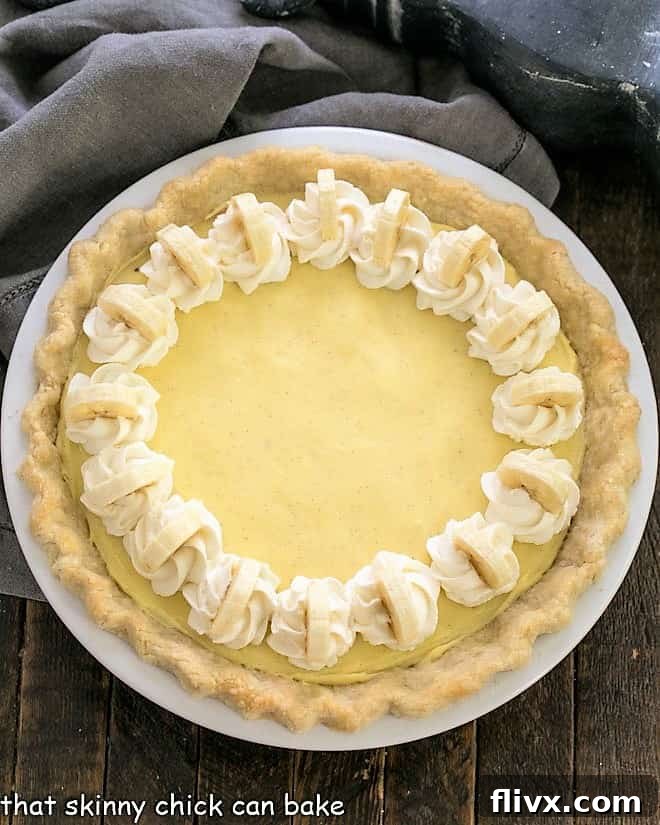Overhead view of a beautiful homemade banana cream pie with whipped cream and fresh banana slices as garnish.