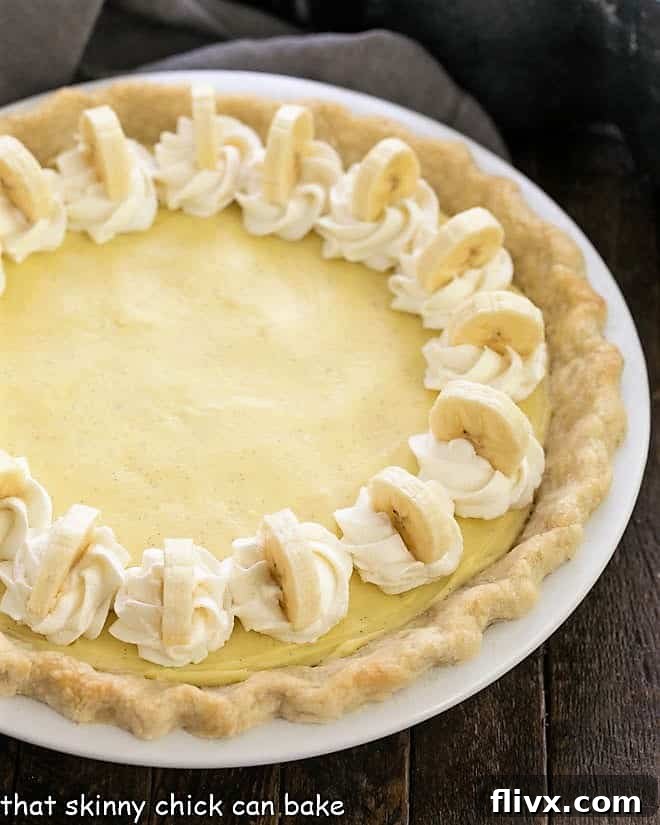 Partial overhead view of a beautifully garnished banana cream pie with fresh whipped cream and banana slices.