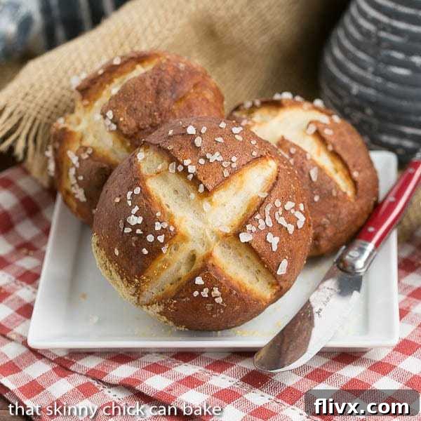 A trio of delicious homemade pretzel rolls artfully arranged on a square white plate, with a red-handled knife suggesting they're ready to be sliced and enjoyed immediately.