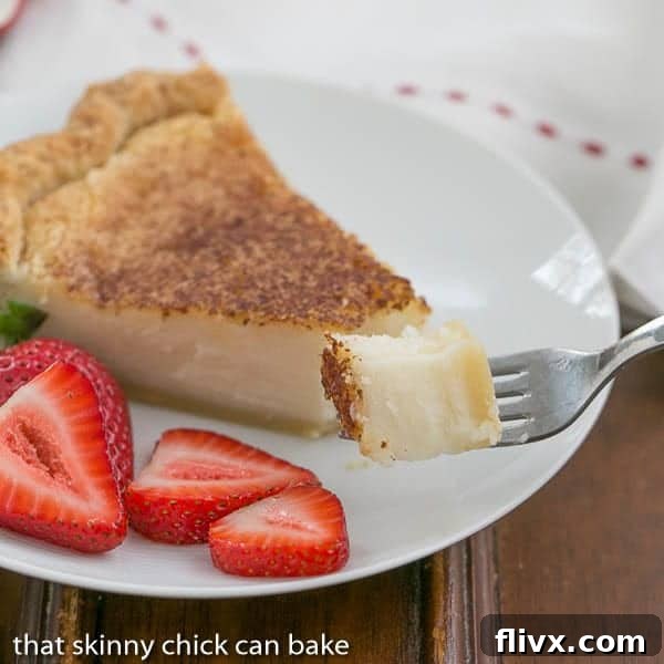 A close-up shot of a Hoosier Sugar Cream Pie bite on a fork, with a blurred pie slice and fresh strawberries visible on a dessert plate in the background.