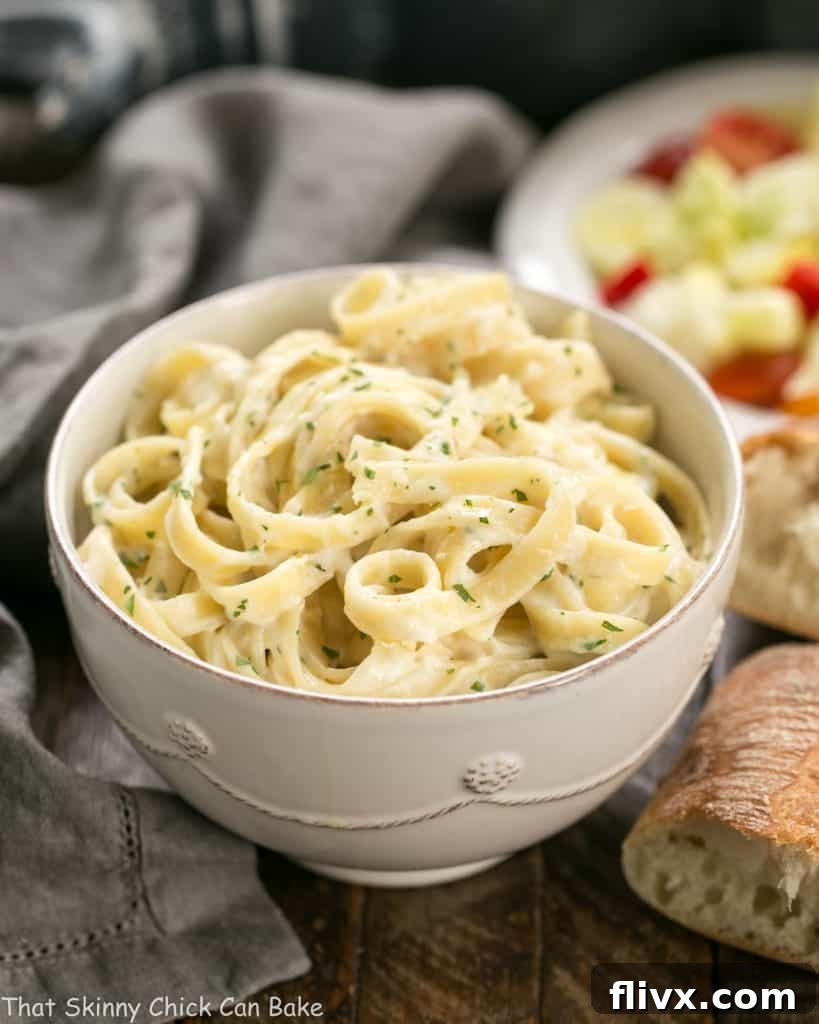 Light Fettuccine Alfredo in a white bowl, served with crusty bread and a fresh salad in the background.