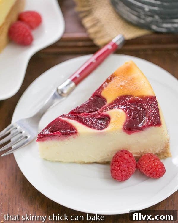 A close-up of a slice of White Chocolate Raspberry Swirl Cheesecake on a white plate, with a red-handled fork resting beside it, highlighting its smooth texture and delicate swirl.