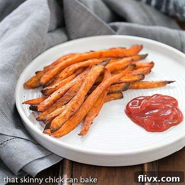 Spicy Sweet Potato Fries served on a white plate with ketchup. Golden orange fries with a dusting of spices, ready to be enjoyed.
