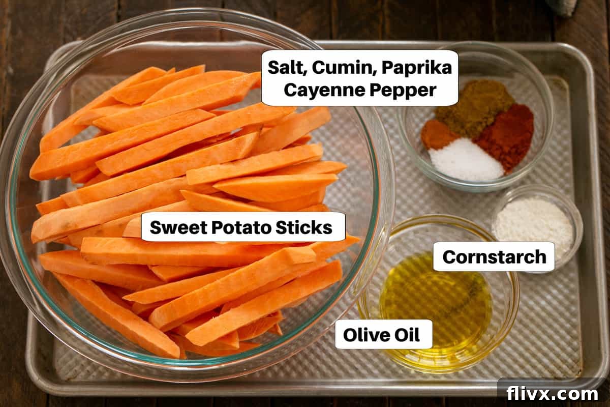 Sweet Potato Fries Ingredients with labels on a sheetpan. Showing olive oil, sweet potatoes, paprika, cumin, cayenne pepper, cornstarch, and salt arranged on a baking sheet.