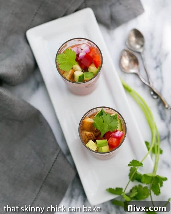 Two Gazpacho Shooters presented on a crisp white rectangular tray, adorned with a fresh sprig of cilantro, highlighting their elegant appeal.