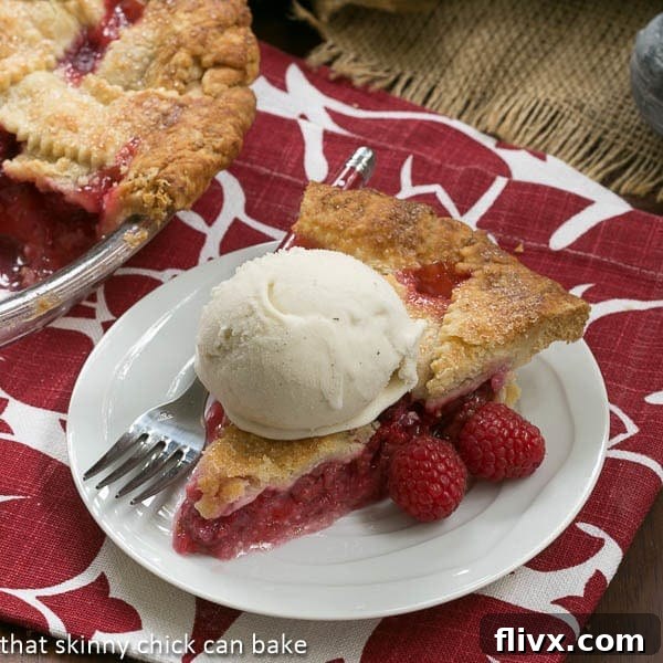 A classic Lattice Topped Raspberry Pie on a white plate, served with a scoop of vanilla ice cream.