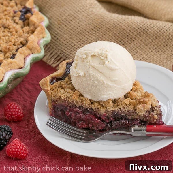 A slice of Razzleberry Pie on a white plate, showcasing its vibrant berry filling and crumb topping.
